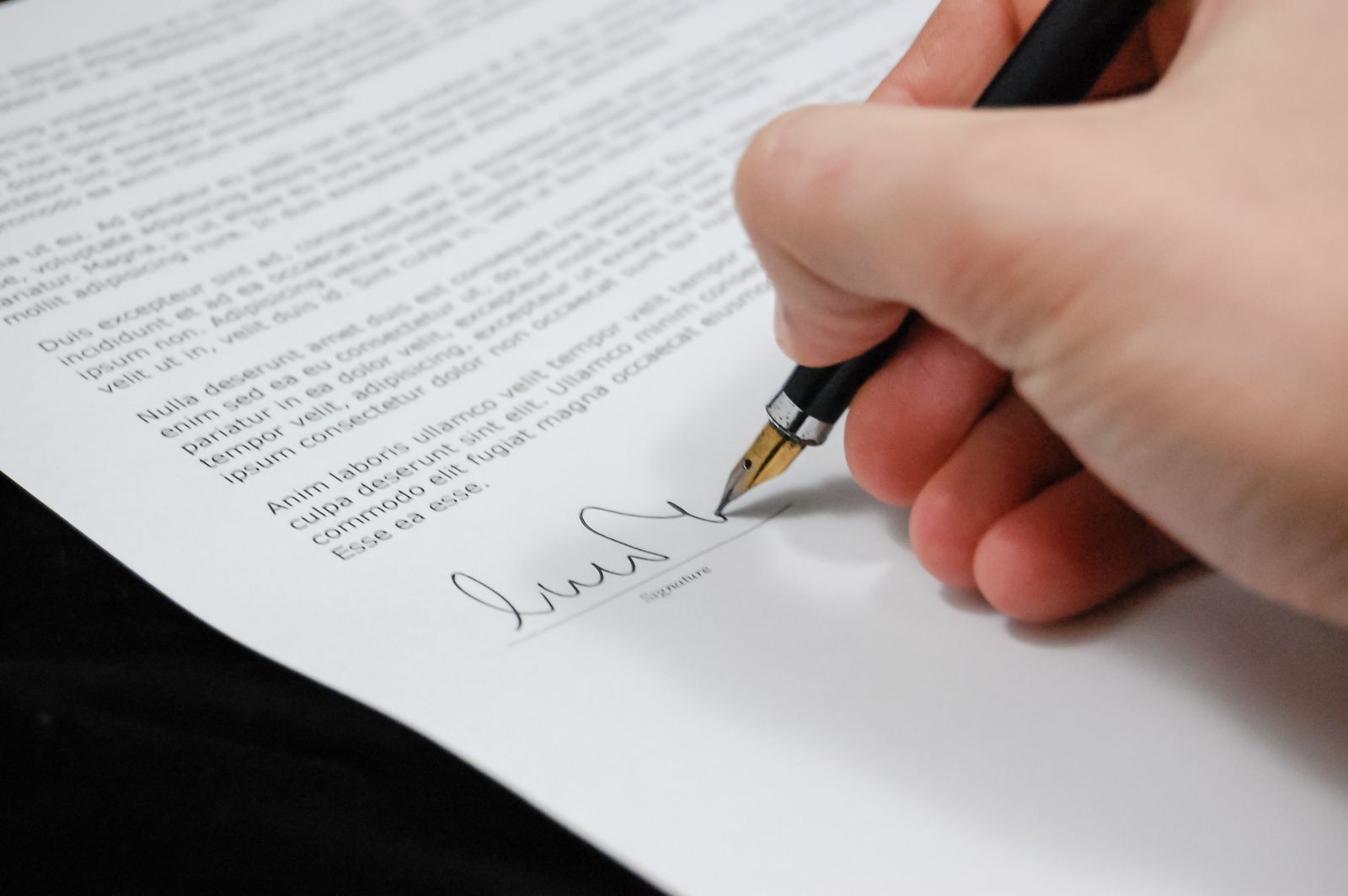 Hand signing official application paperwork with a fountain pen